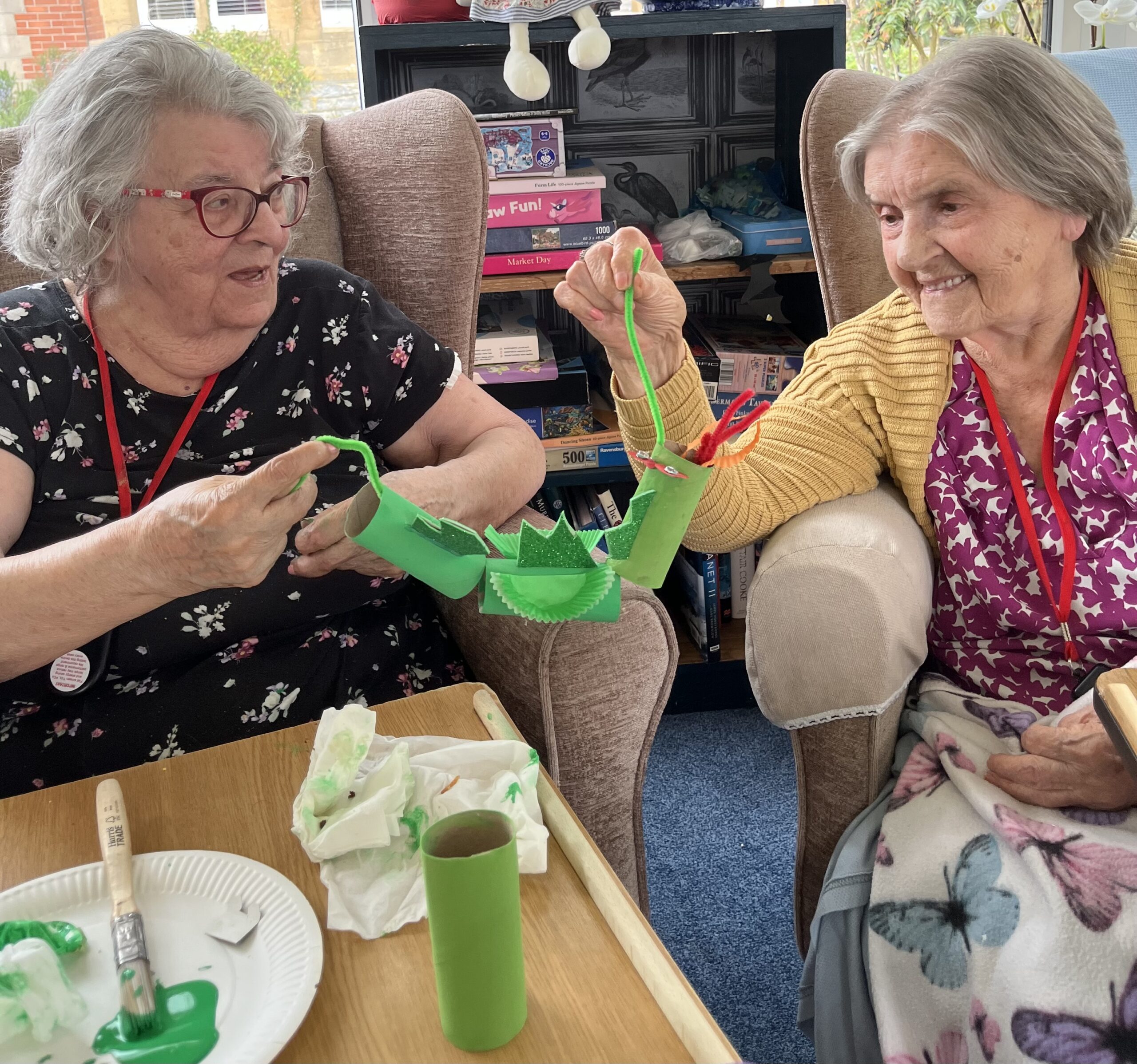 Maggie and Herta talking about a dragon holding each end of a pipe cleaner scaled