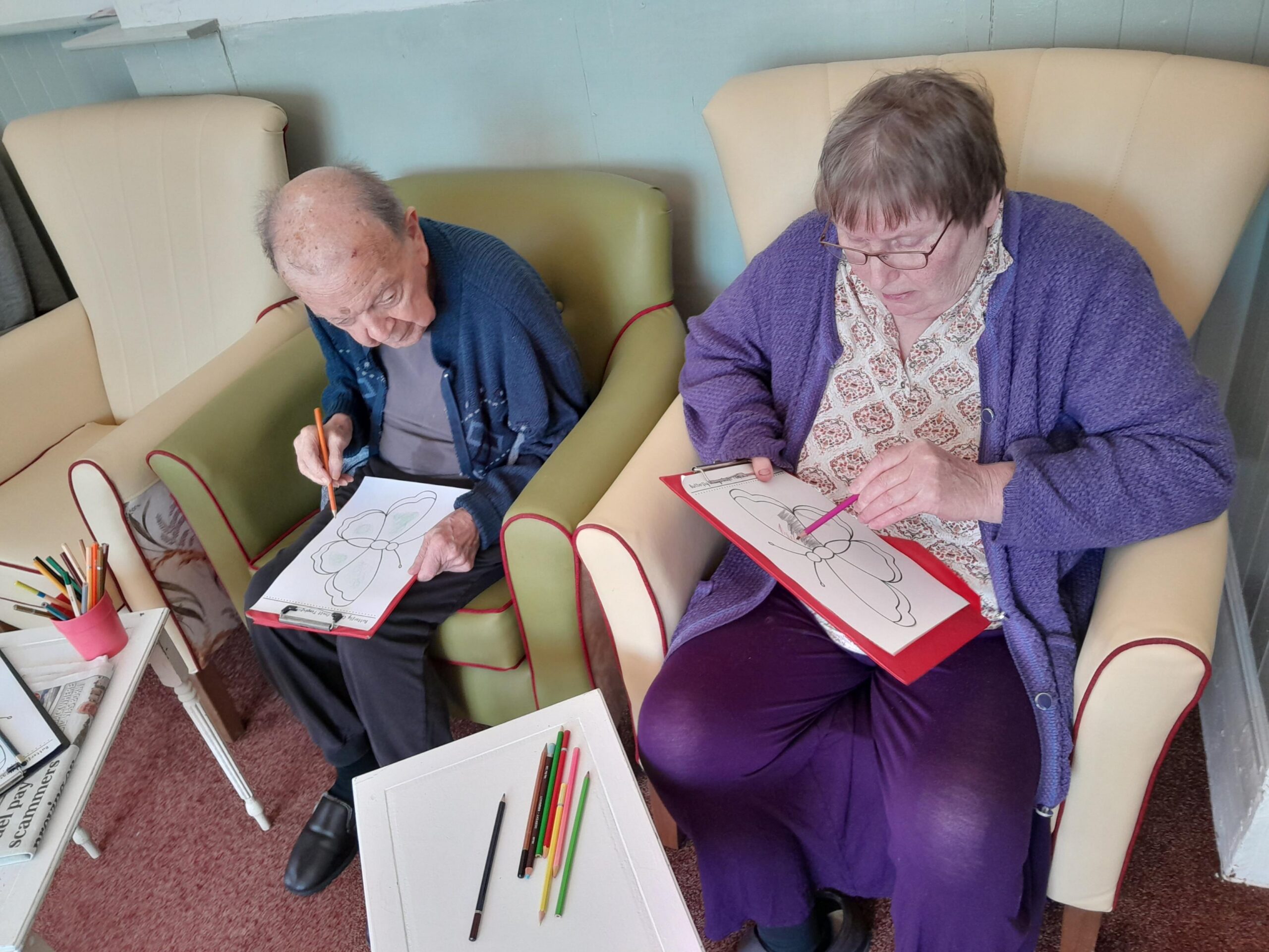 Male and female residents seated together colouring in butterflies scaled