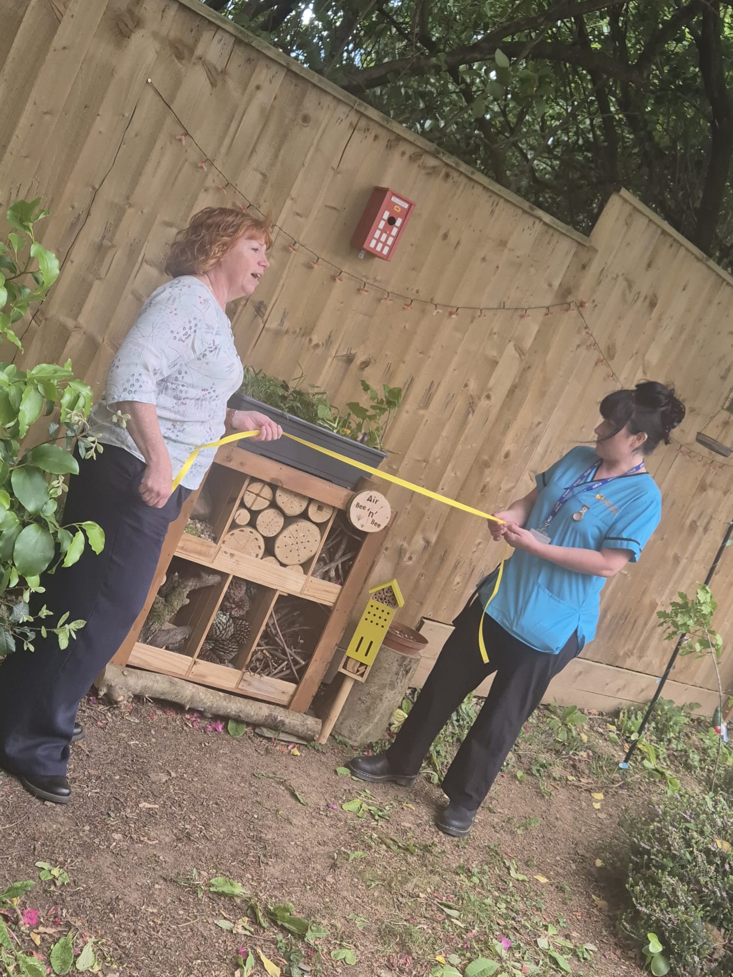 Amanda and Billie holding a yellow ribbon in front of the Air Bee n Bee