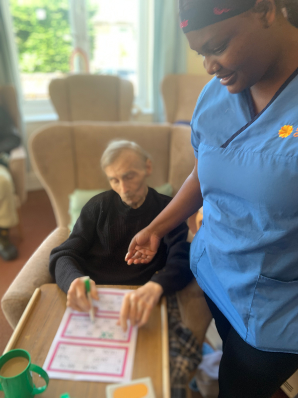 Carer stood with a seated male resident looking at his bingo sheet