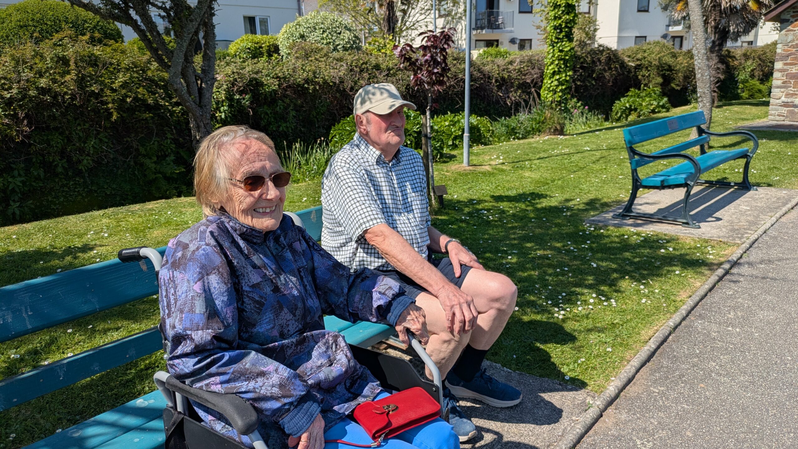 Cecily in her wheelchair and Dave seated on a bench in a park scaled