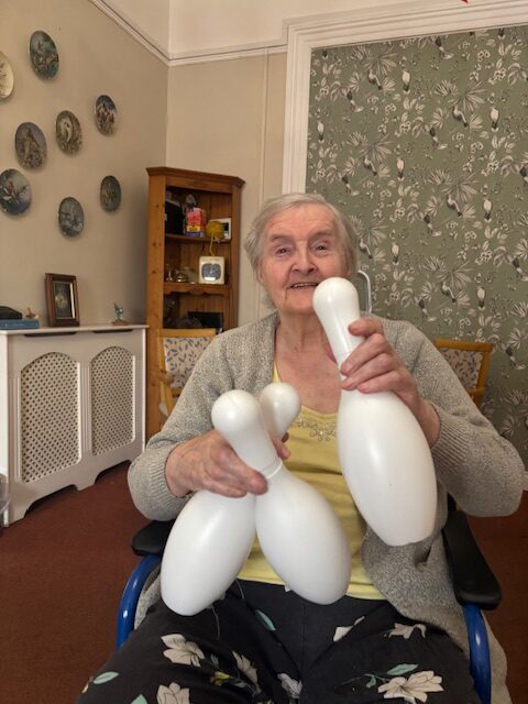 Female resident Doris in a wheelchair holding up a bowling pin smiling rotated