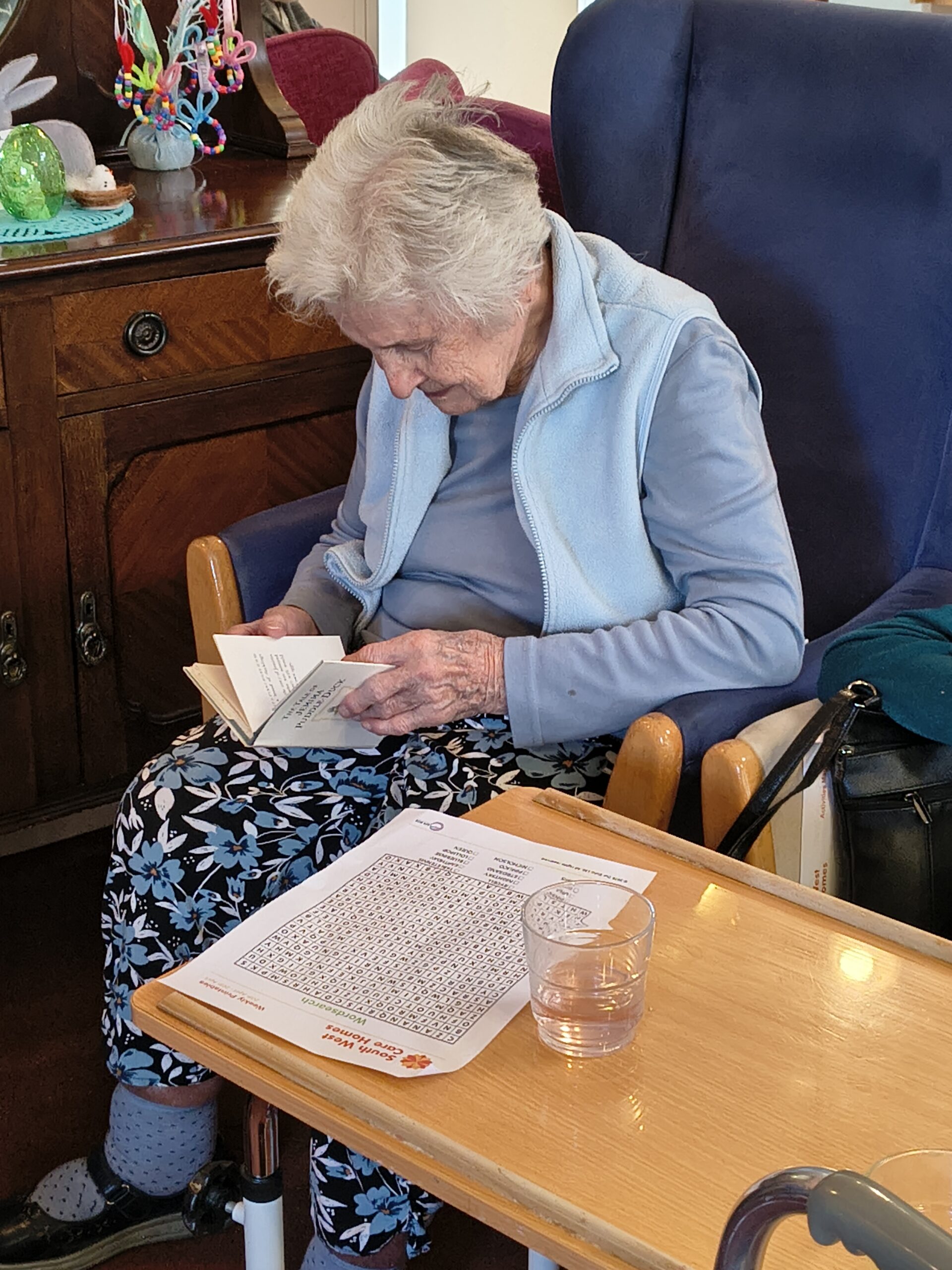 Female resident looking at Jemima Puddle Duck book with word search sheet scaled