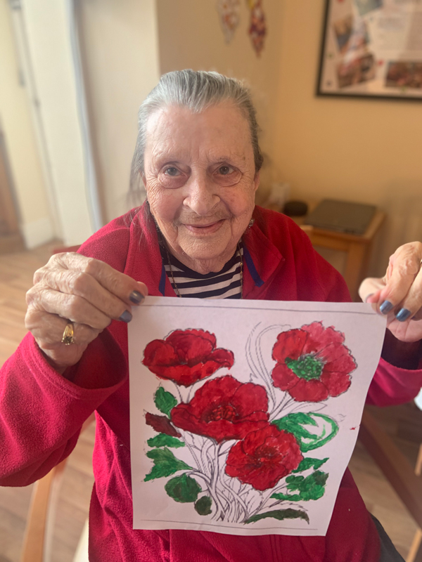 Female resident proudly holding up her finished picture of poppies smiling