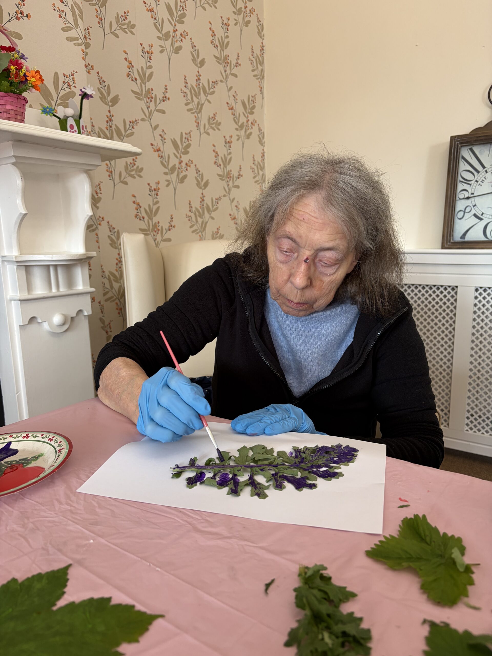 Female resident seated at a table painting leaves and using them as stamps to create a picture scaled