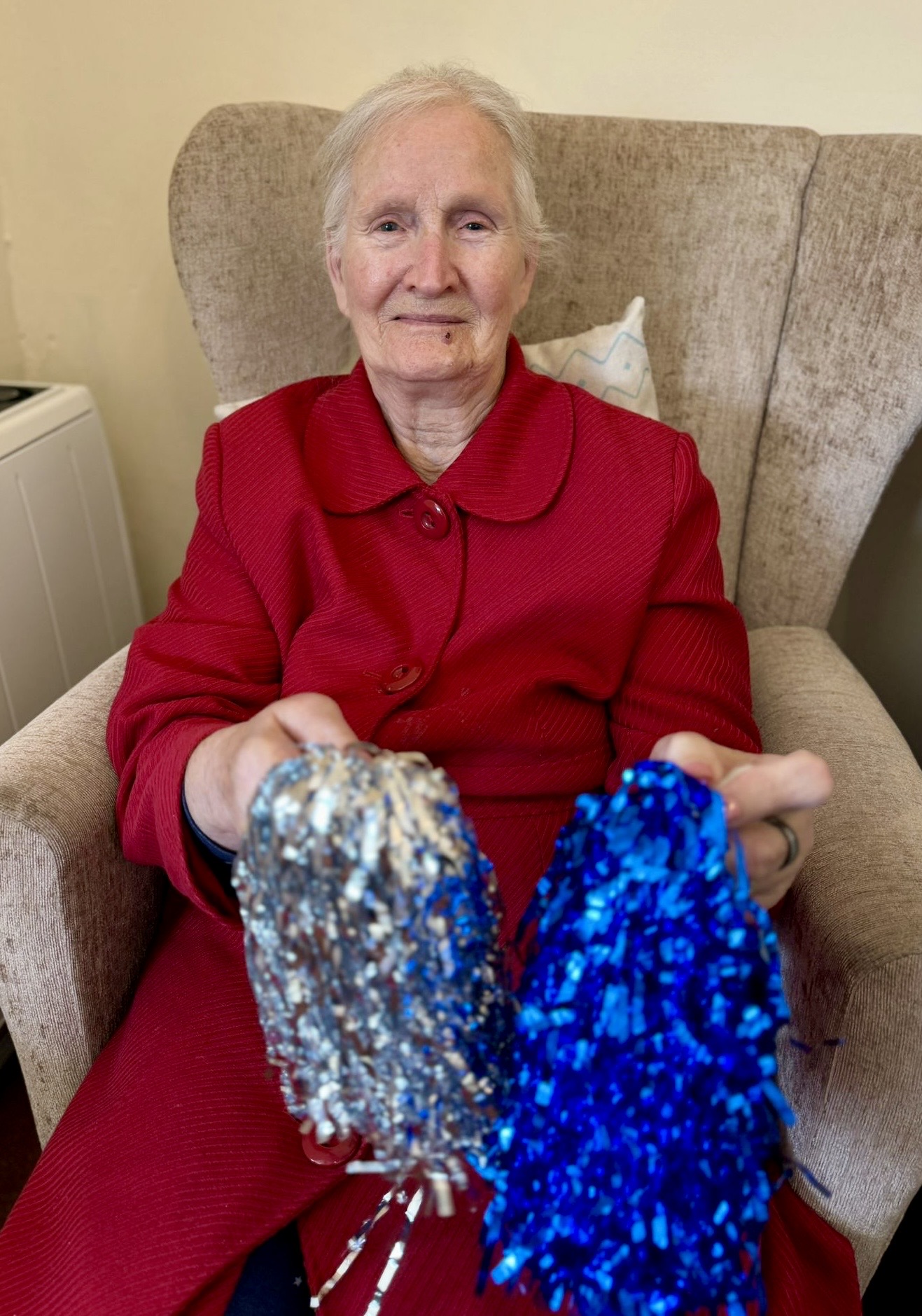 Female resident seated holding a blue and a silver shiny pompoms