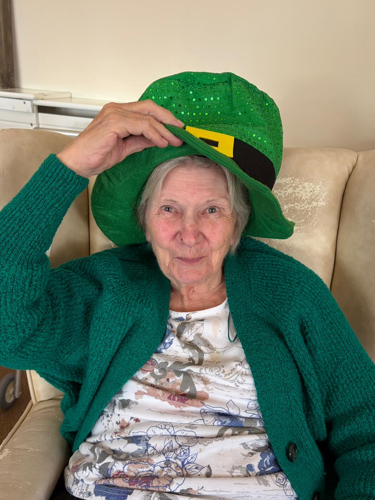 Female resident seated smiling as she tips her leprechaun hat in greeting