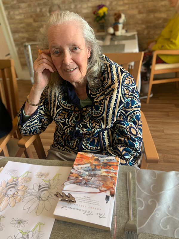 Female resident smiling at the camera with her colouring sheet on the table in front of her