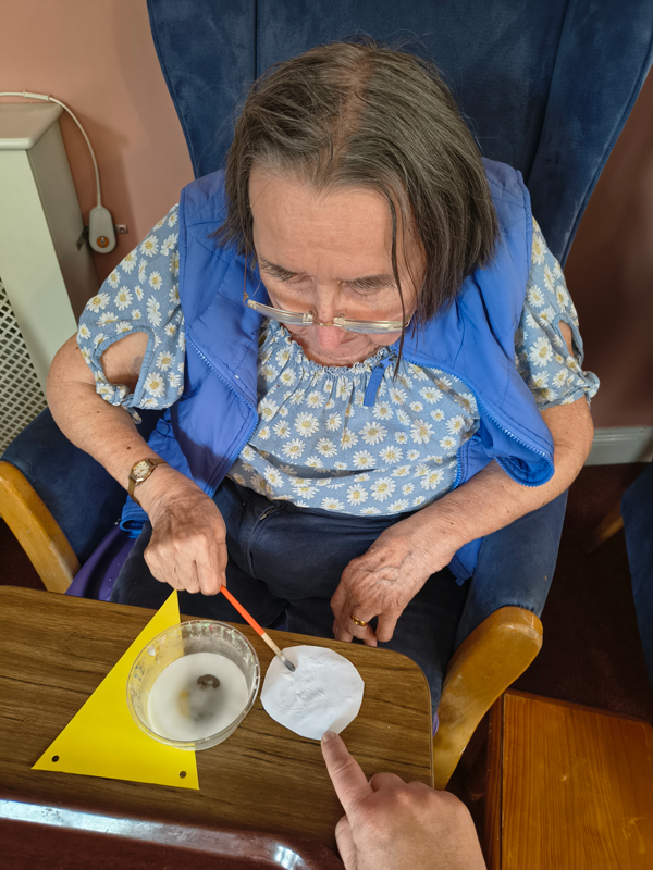 Female resident using a brush to put glue onto paper picture for the bunting