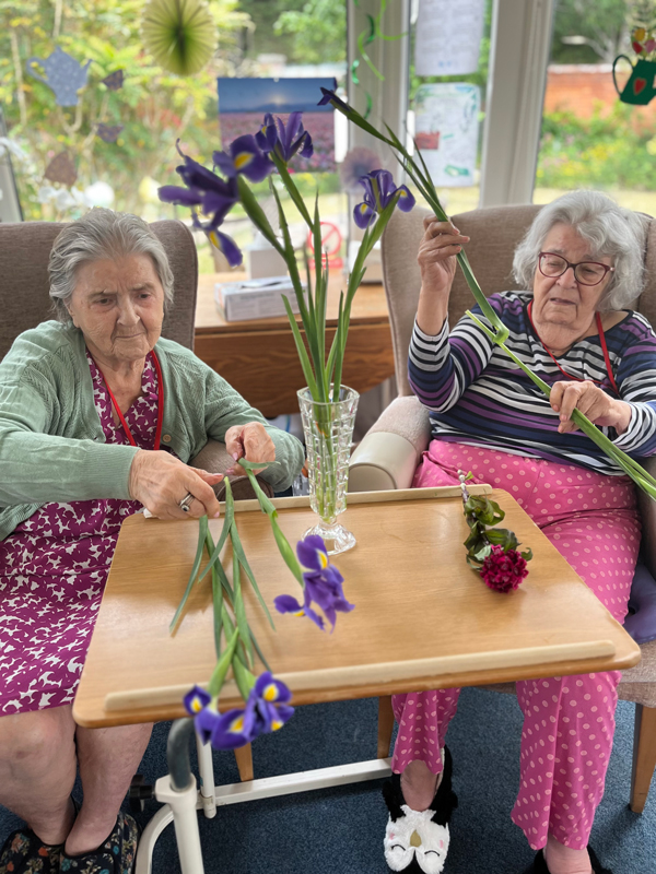Herta and Maggie working together putting flowers in a vase