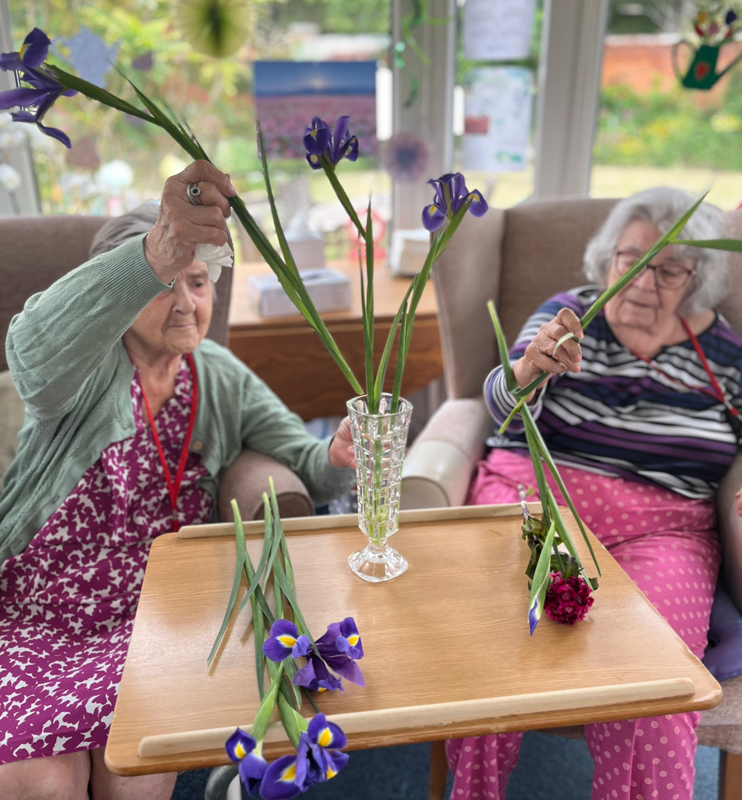 Herta putting flowers in a vase while Maggie cuts them