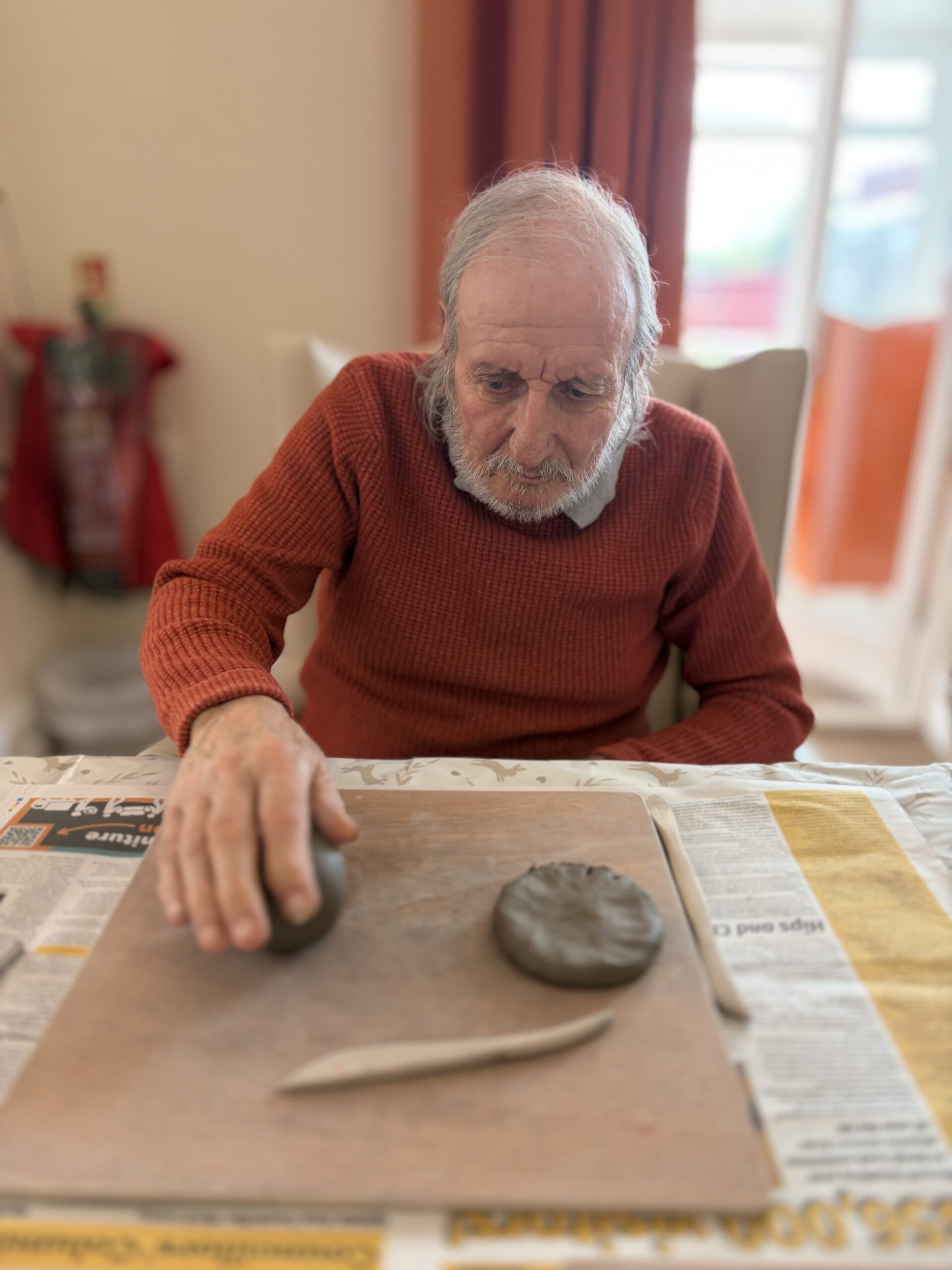 Male resident flattening a piece of clay with his hand scaled