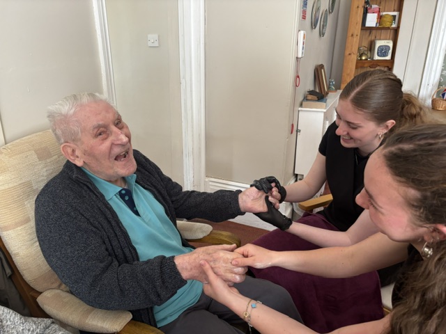 Male resident having both hands massaged by two students all laughing and smiling