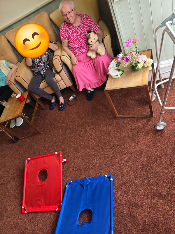 Marcia having a go throwing a blue bean bag towards a tilted mat with a hole