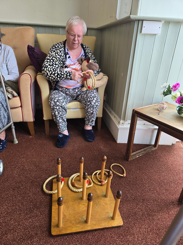 Marcia seated having a go throwing rope rings onto a board of wooden pegs on the floor