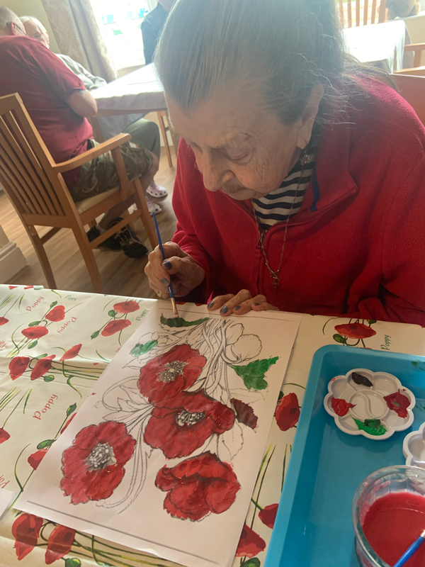 Resident seated using paint to colour in a picture of poppies