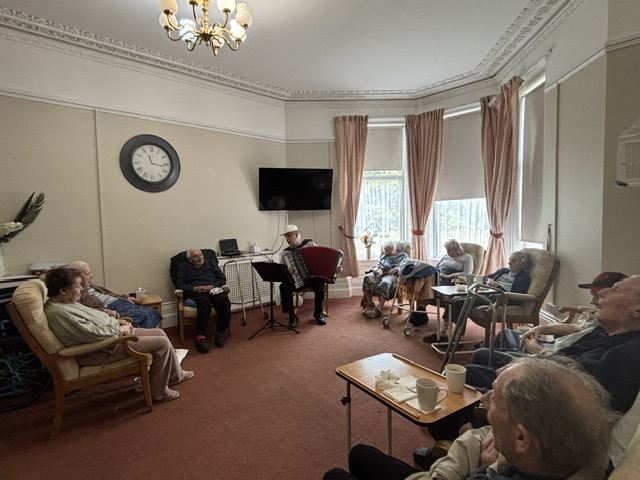 Residents seated around Bing playing accordion