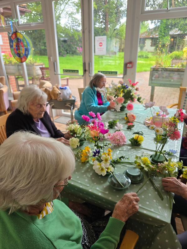 Residents seated together around a table filled with flowers that the residents are placing into foam bases