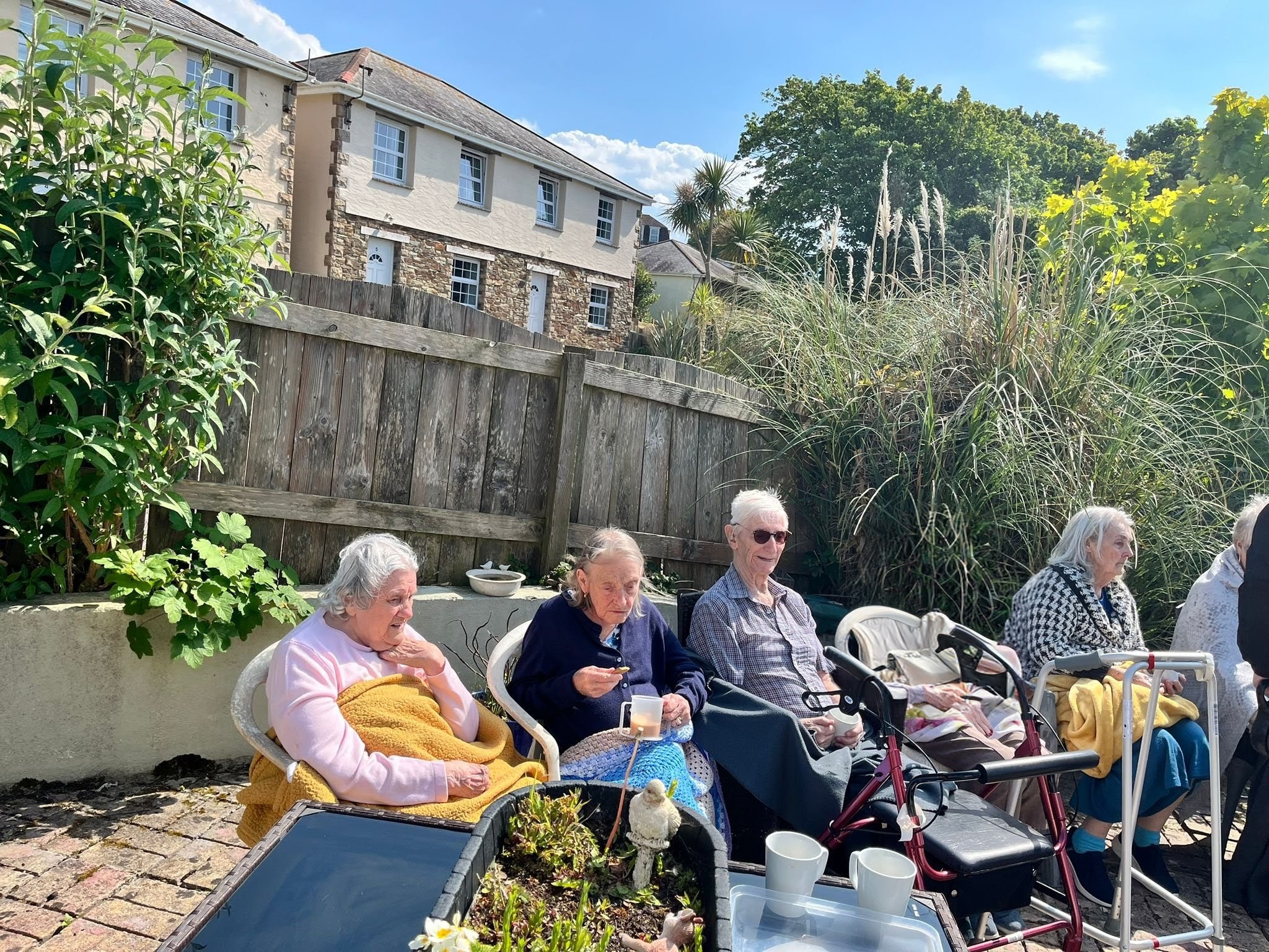 Residents seated together outside in the sunshine with tea and biscuits