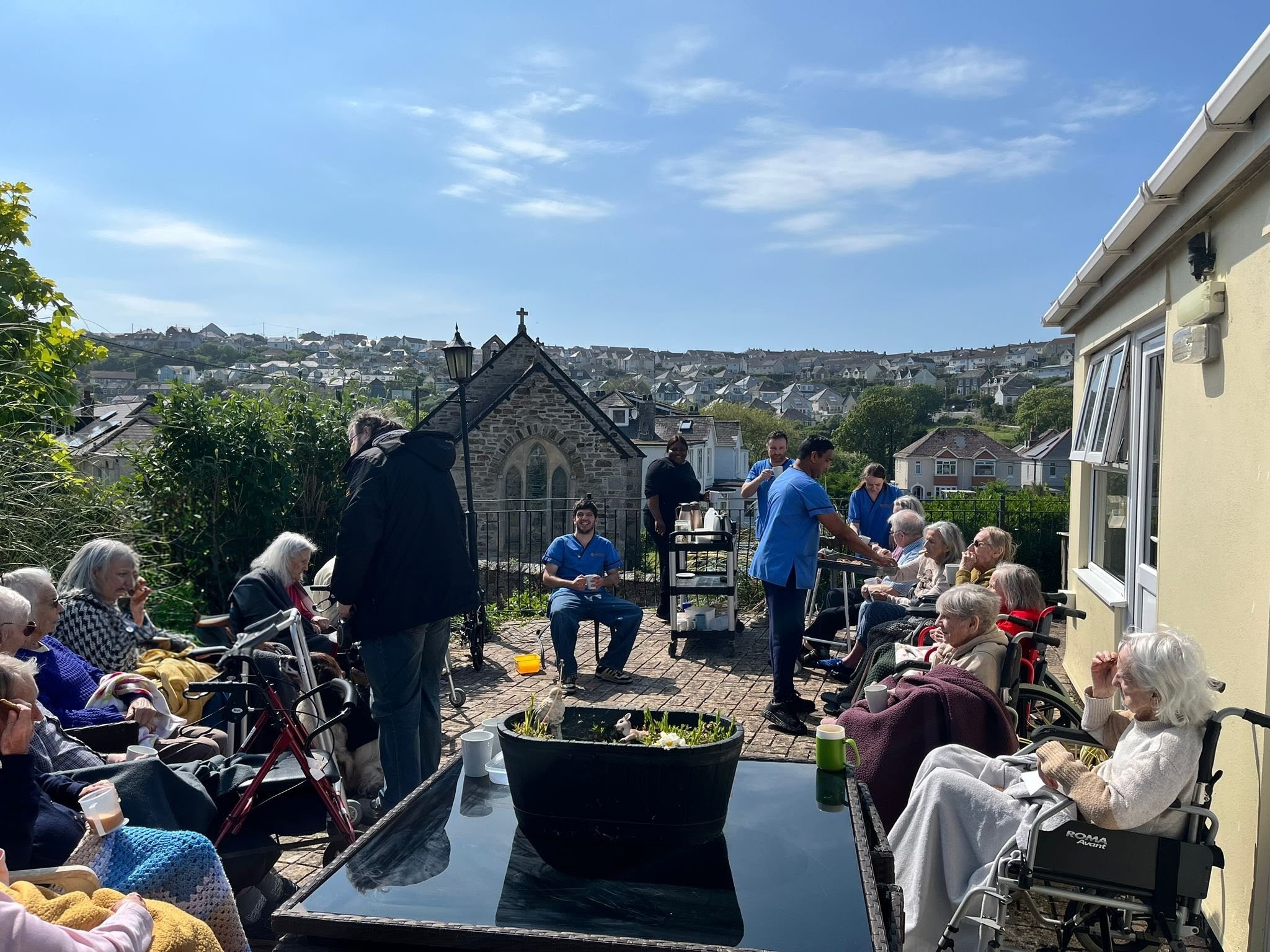 Residents seated together outside in the sunshine with view over Perranporth