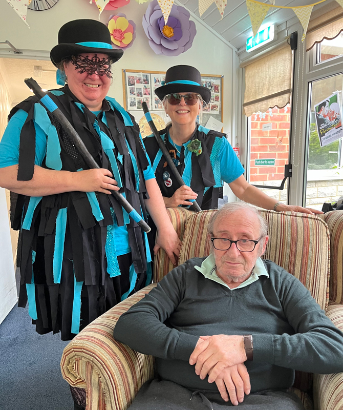 Robin seated with two morris dancers in blue and black standing behind him