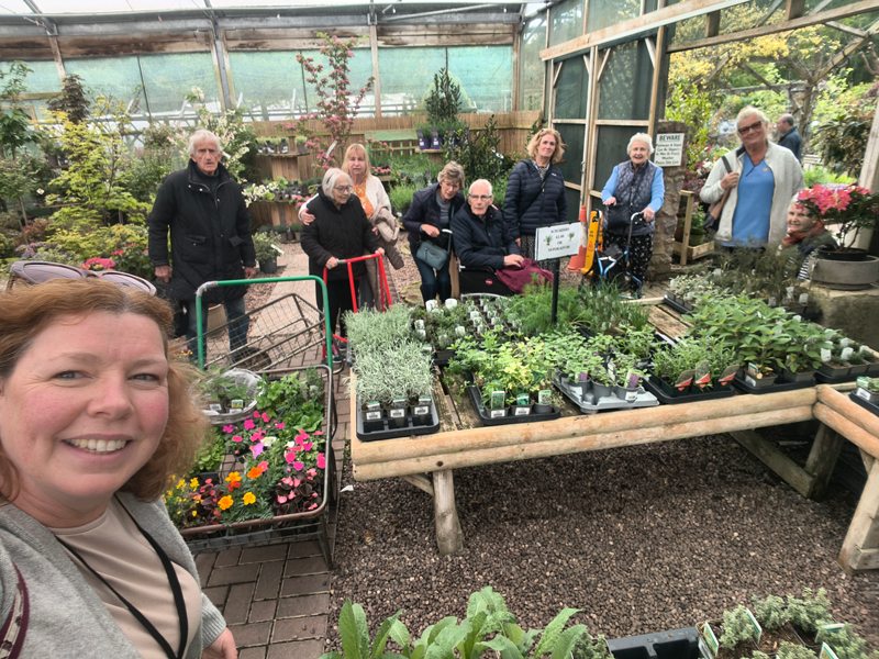 Selfie with residents in the background standing behind pots of plants
