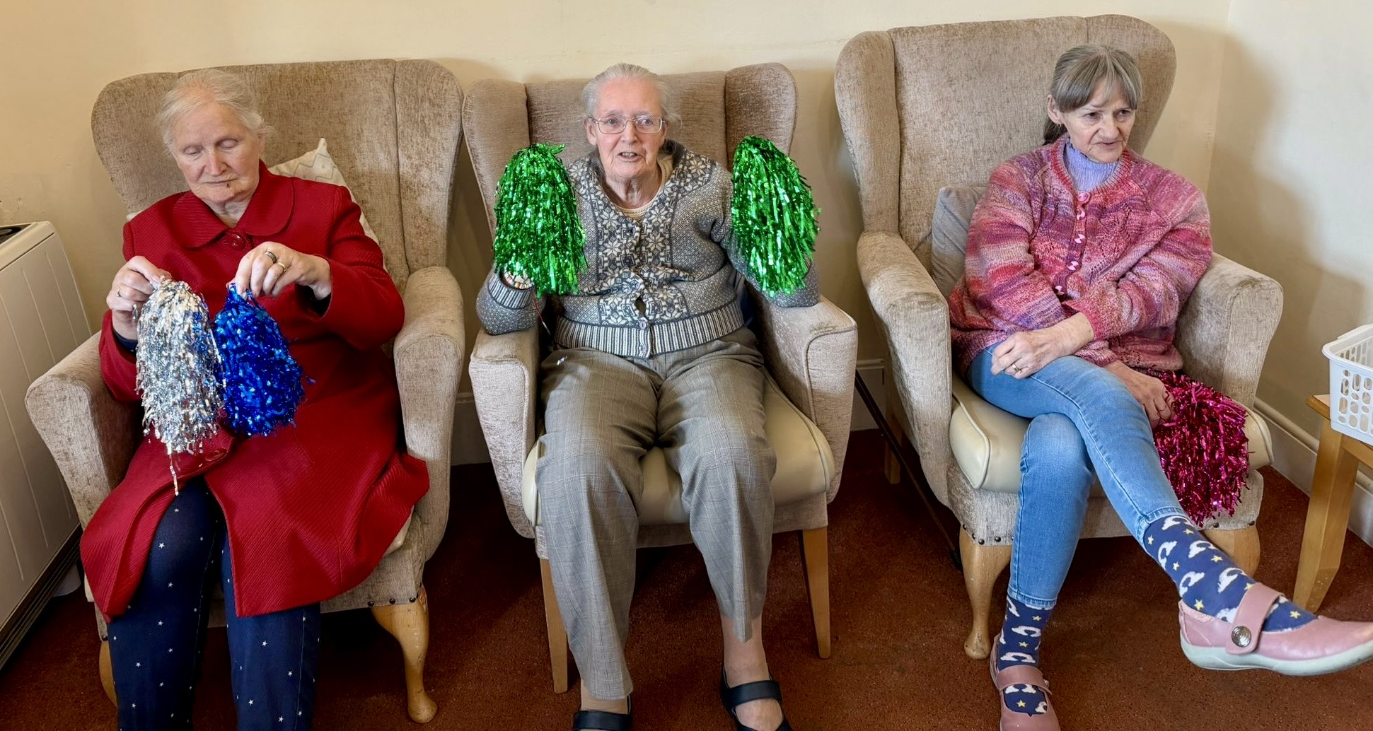 Three Female residents seated in a row waving their pompoms