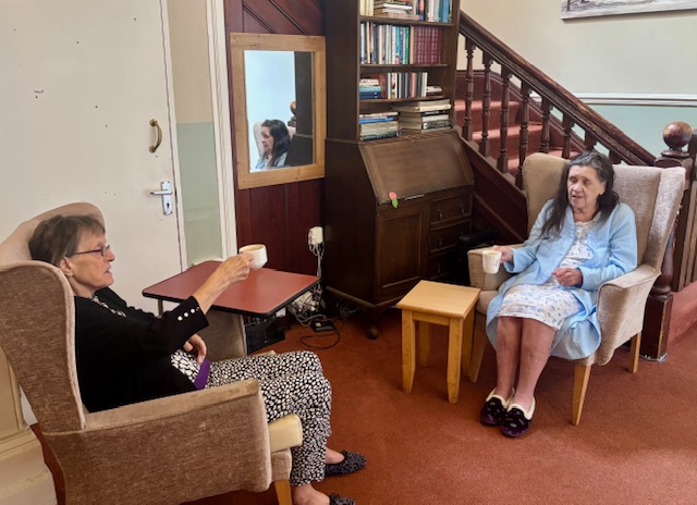 Two female residents seated together with cups of tea