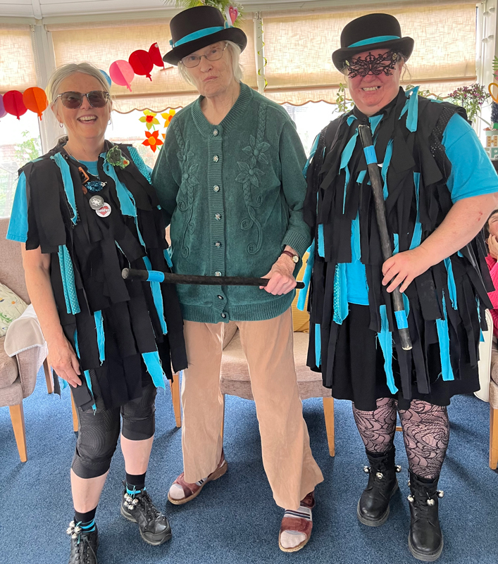 Wendy with a Morris hat on and stick stood between two Morris dancers
